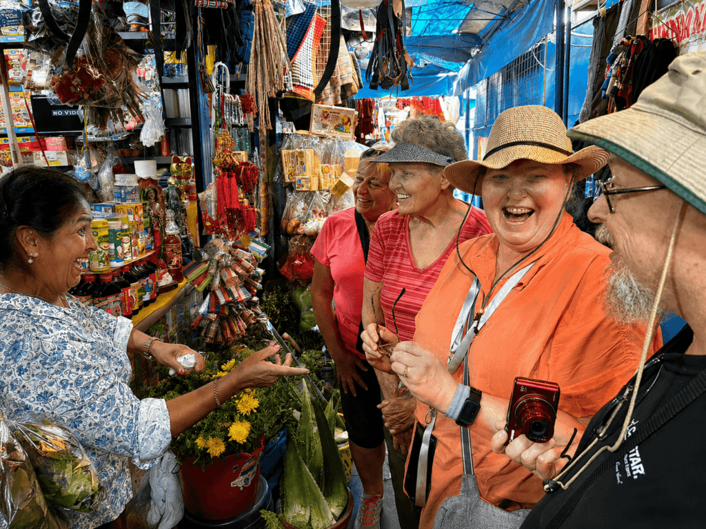 Two happy international tourists smiling and interacting with a local market vendor during an authentic culinary experience in Lima, Peru.