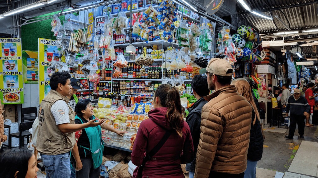 Lima Tasty Tours guide explaining local products to international travelers at a traditional neighborhood market stall in Lima, Peru.⁠