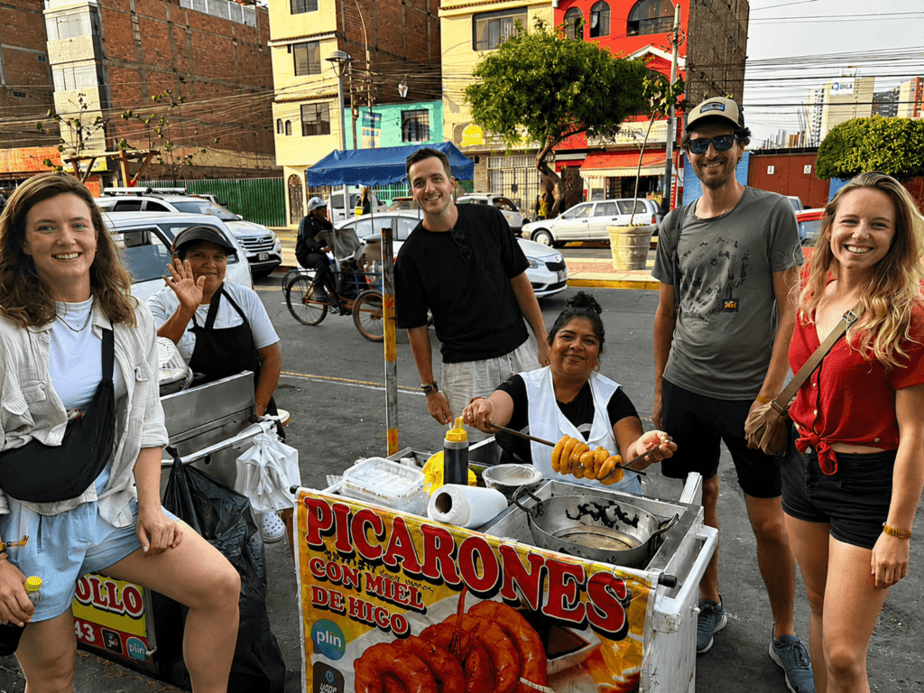 ⁠International travelers enjoying authentic handmade picarones at a traditional street food cart with Lima Tasty Tours in Lima, Peru.⁠